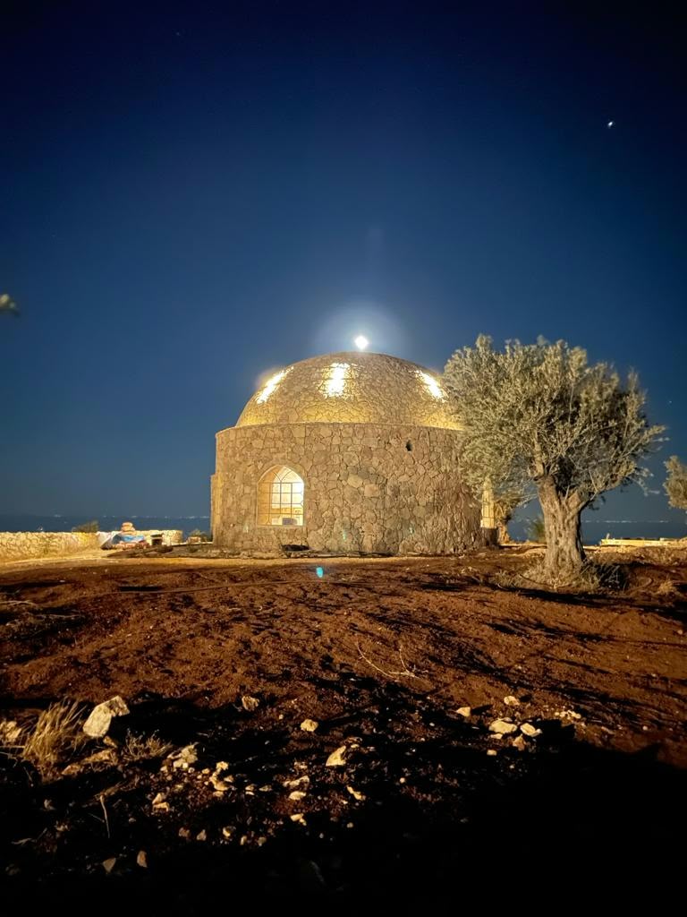 The illuminated prayer house beside an olive tree at night